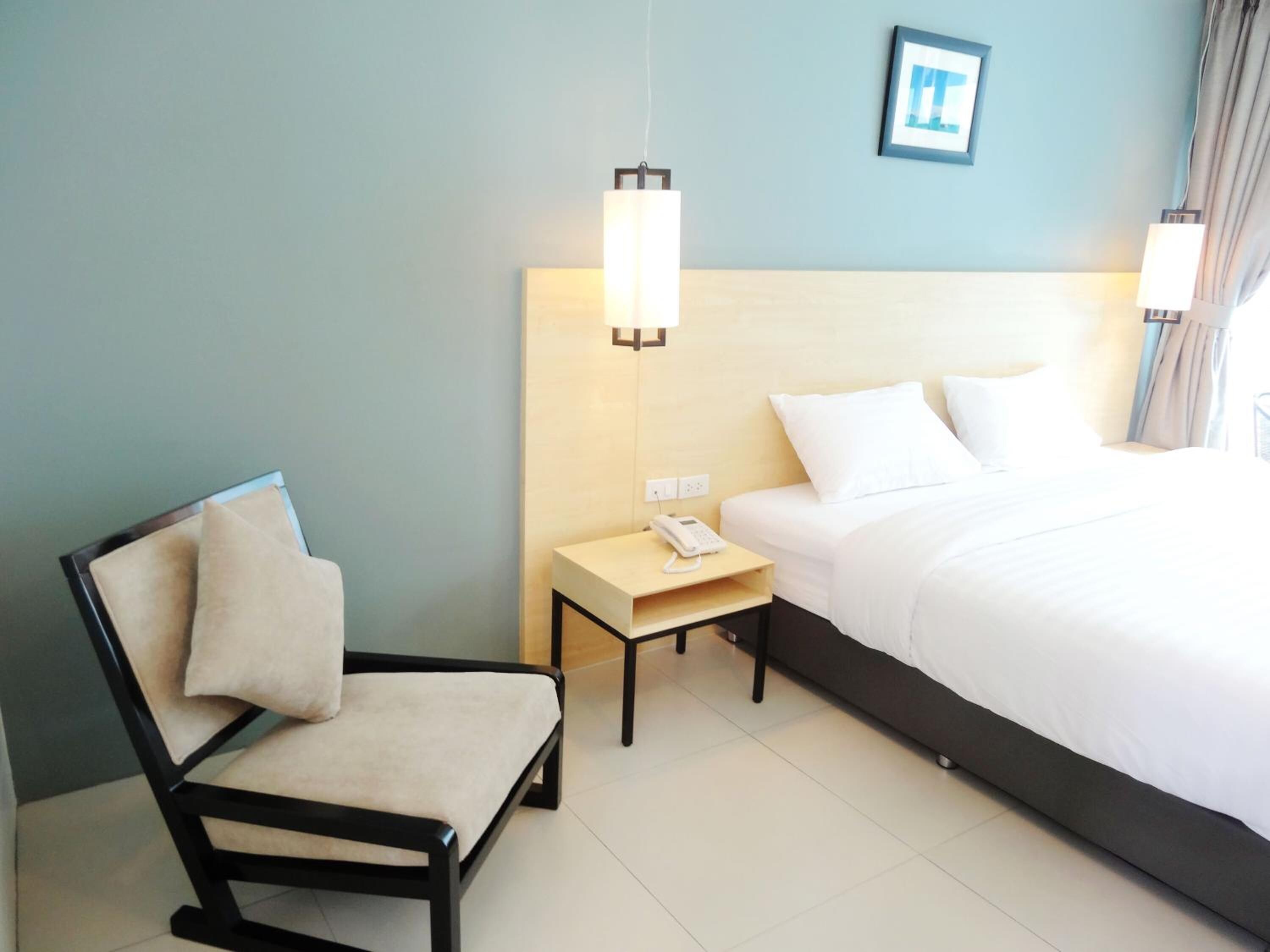 Une chambre d’hôtel comprenant un lit, une chaise, une table de chevet avec un téléphone et un luminaire fixé au mur.