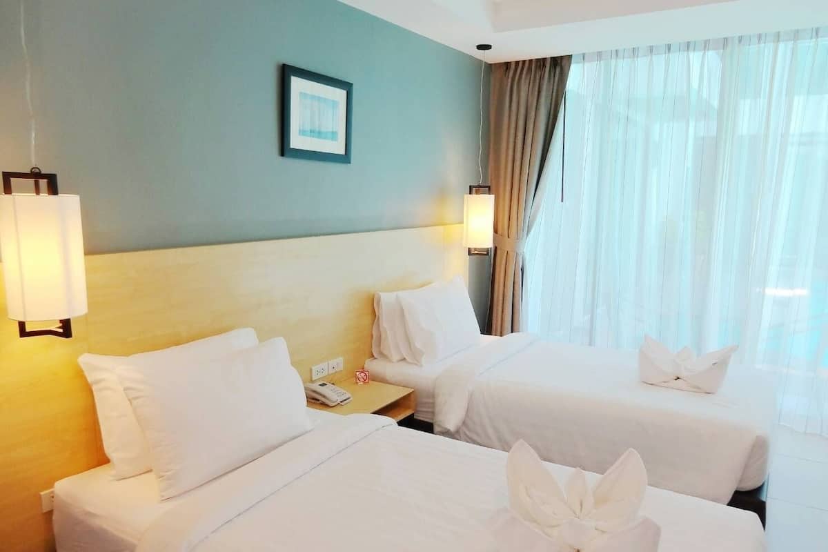 Habitación de hotel con dos camas, cabecera, mesita de noche con teléfono, lámpara y ventana con cortinas.