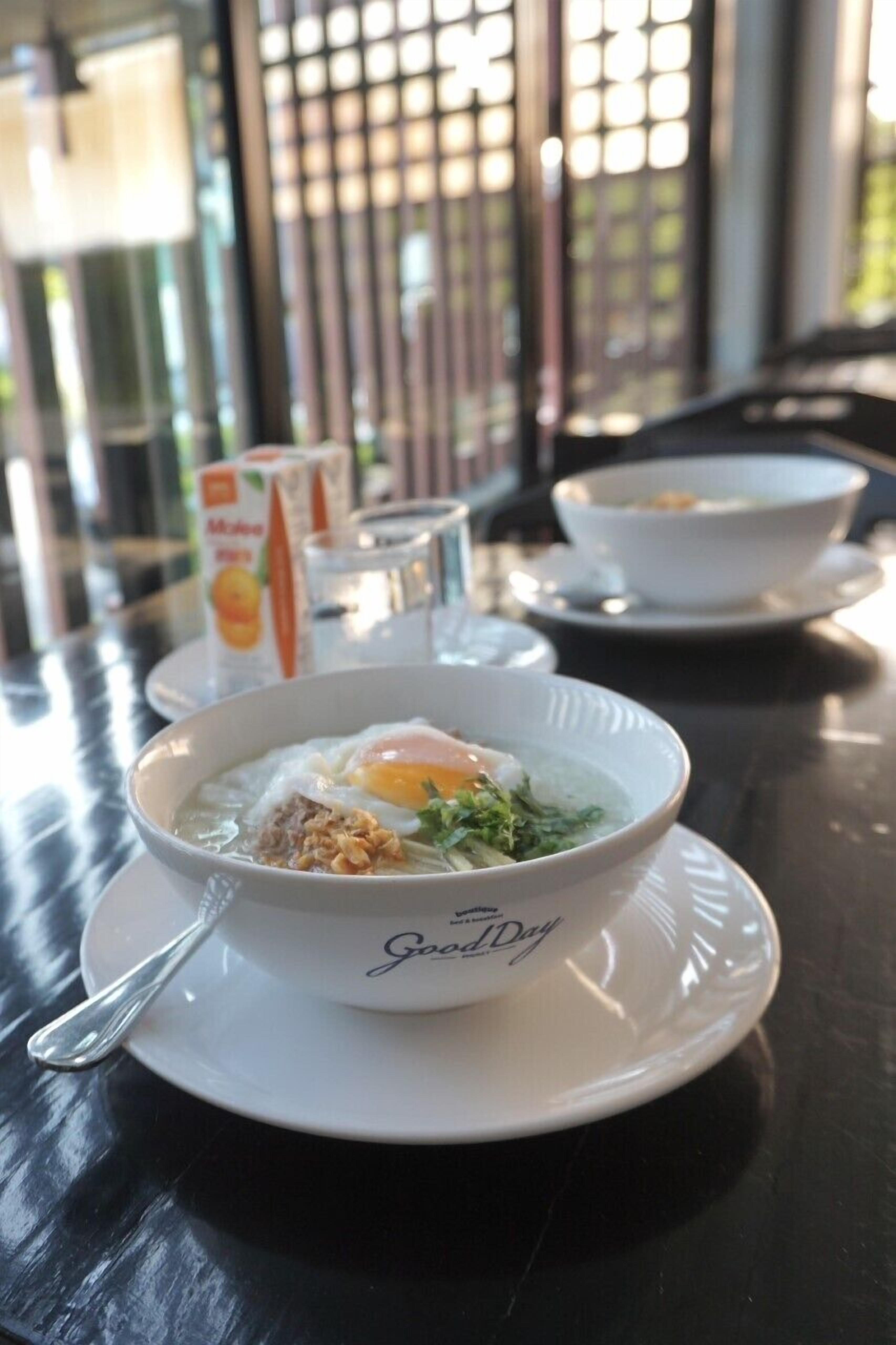 A bowl of food on a table with a spoon, a glass of water, and a carton of orange juice.