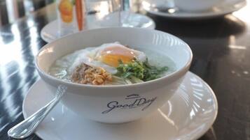 A bowl of food on a table with a spoon, a glass of water, and a carton of orange juice.