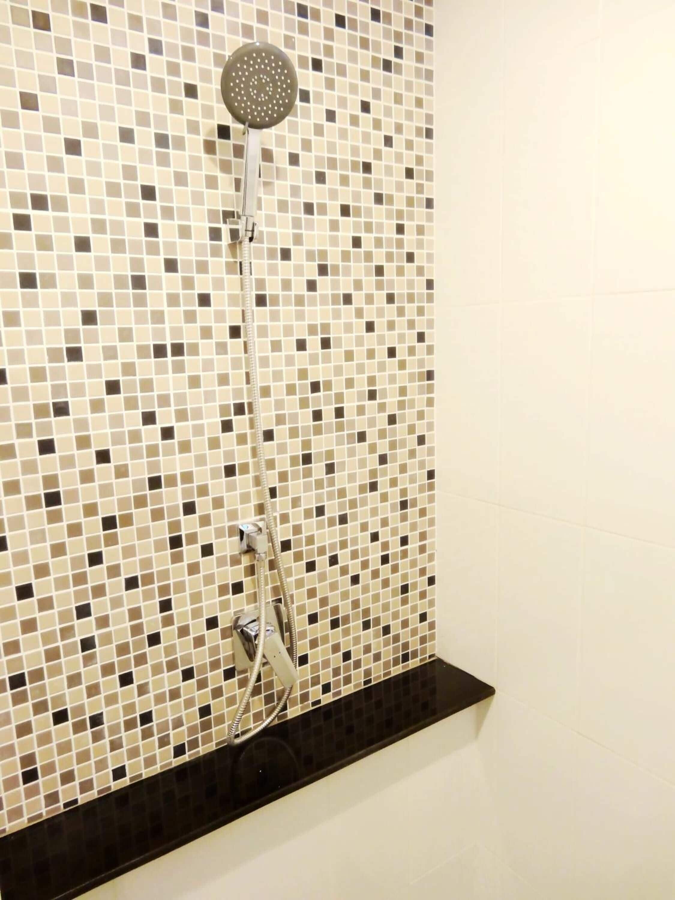 A shower with a mosaic tile wall and a black shelf below.
