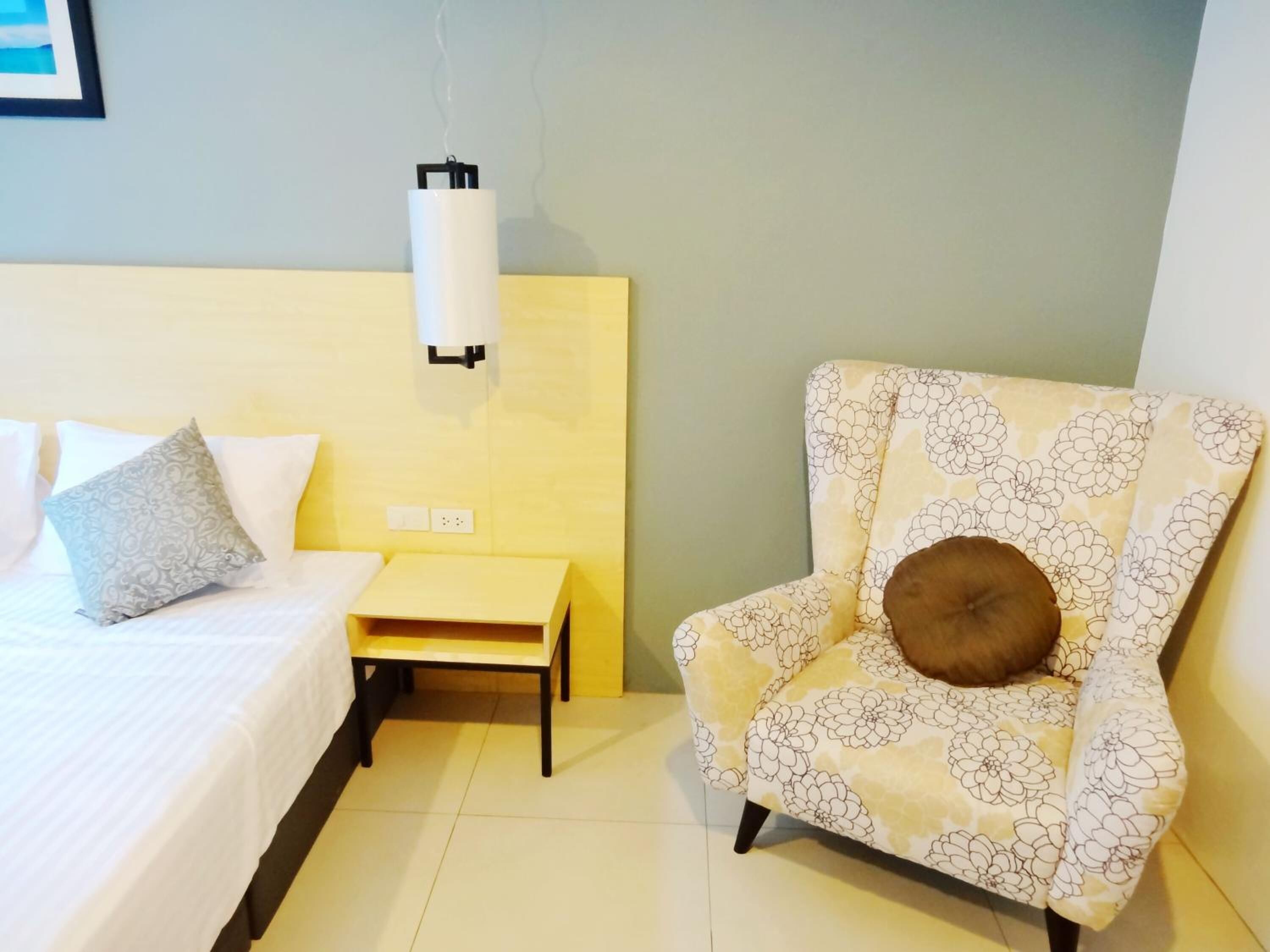 Una habitación de hotel con cama, mesita de noche, silla y lámpara de pared.