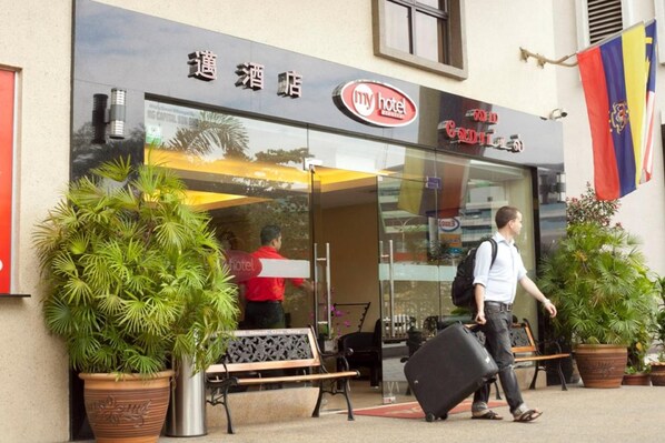 A hotel entrance with a glass door, a bench outside, and potted plants.