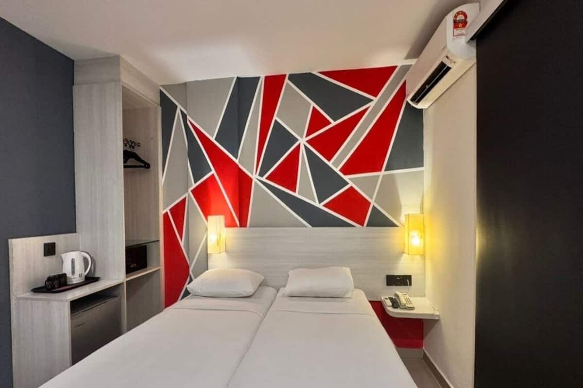 A hotel room with a bed, bedside tables, a desk with a kettle, and a geometric wall design.