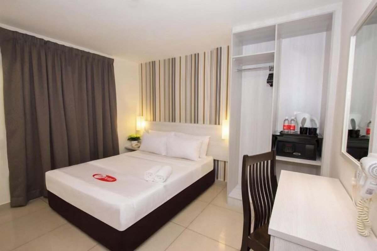 Habitación de hotel con cama, escritorio, silla, armario y espejo.