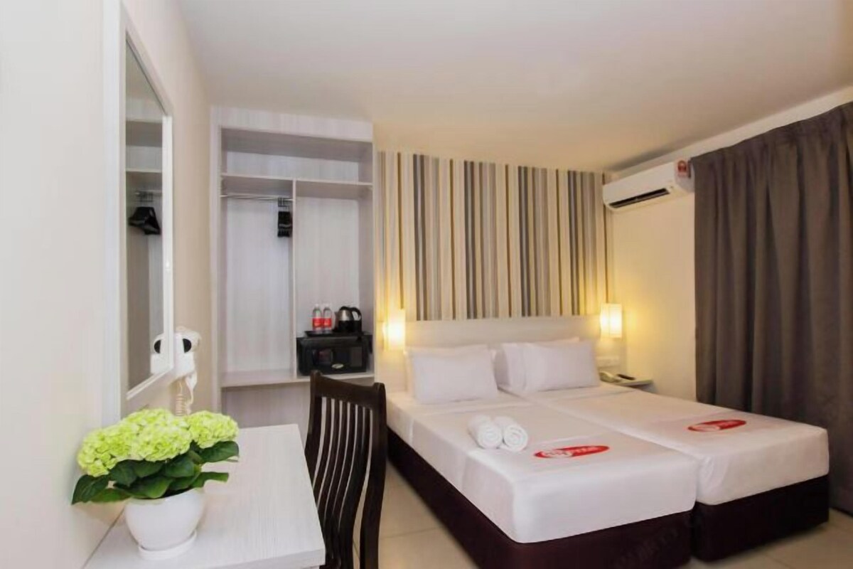 A hotel room with two beds, a desk, a chair, a mirror, a wardrobe, and a potted plant.