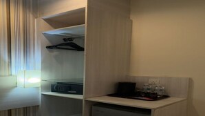 A compact room with a built-in microwave, a small refrigerator, and a shelf with a black appliance and a water bottle. - My Hotel @ Sentral (Kuala Lumpur)