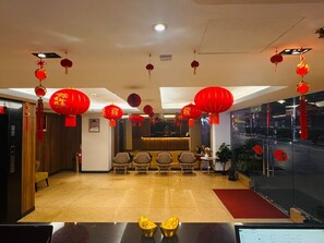 A hotel lobby with red lanterns, a reception desk, seating area, and a reception counter.