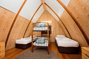 A cozy attic bedroom with wooden walls, a bunk bed, and two single beds.