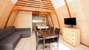 Una habitación acogedora con paneles de madera, una cama entrepiso, un sofá, una mesa de comedor y un televisor.