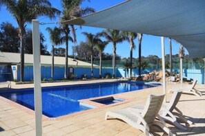 A swimming pool with lounge chairs, palm trees, and a covered area.