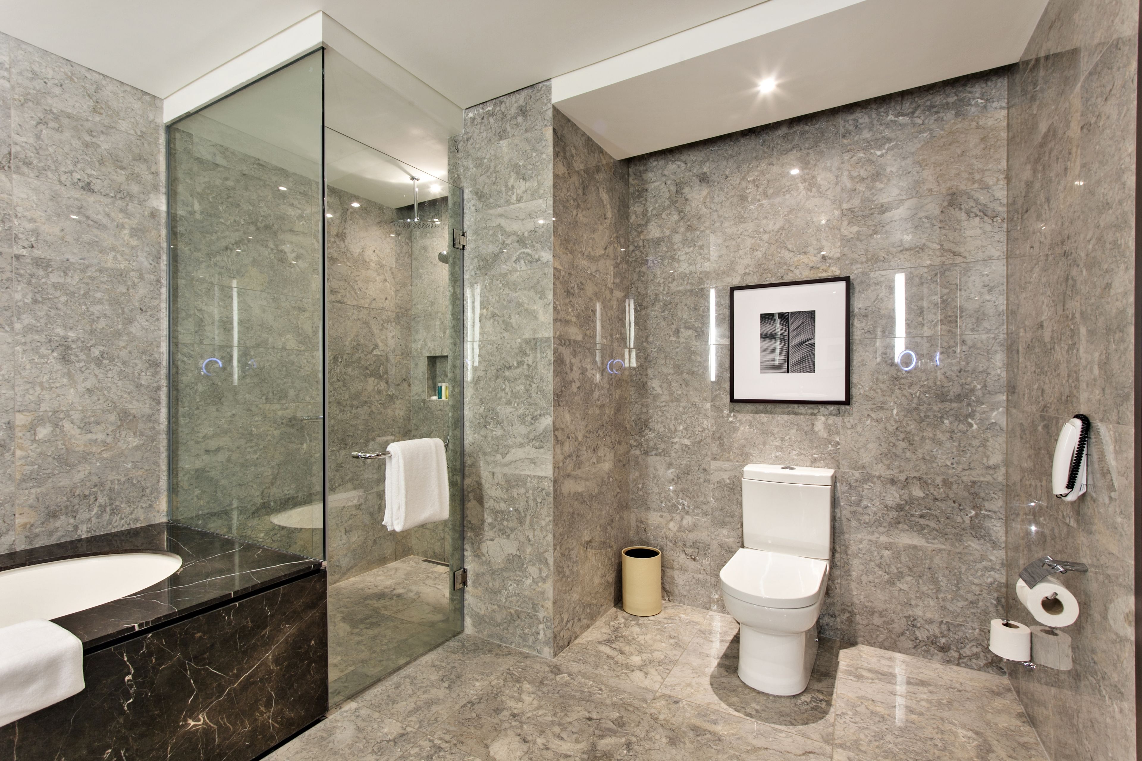 A modern bathroom with a glass-enclosed shower, a marble sink, and a toilet with a framed picture above it.