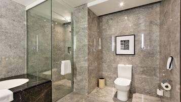 A modern bathroom with a glass-enclosed shower, a marble sink, and a toilet with a framed picture above it.