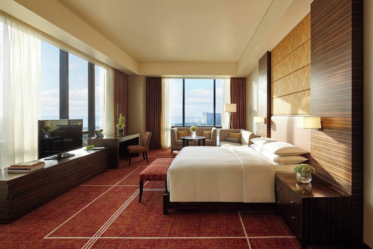 Ein Hotelzimmer mit einem großen Bett, einem Schreibtisch mit Fernseher, einer Sitzecke mit Tisch und Blick auf die Stadt.