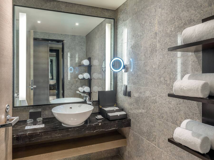 A modern bathroom with a large mirror, a round mirror, a white sink, and shelves with towels.