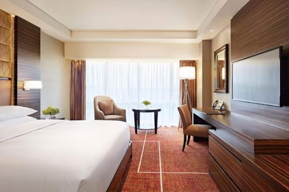 A hotel room with a large bed, a desk, a chair, a TV, and a window with curtains.