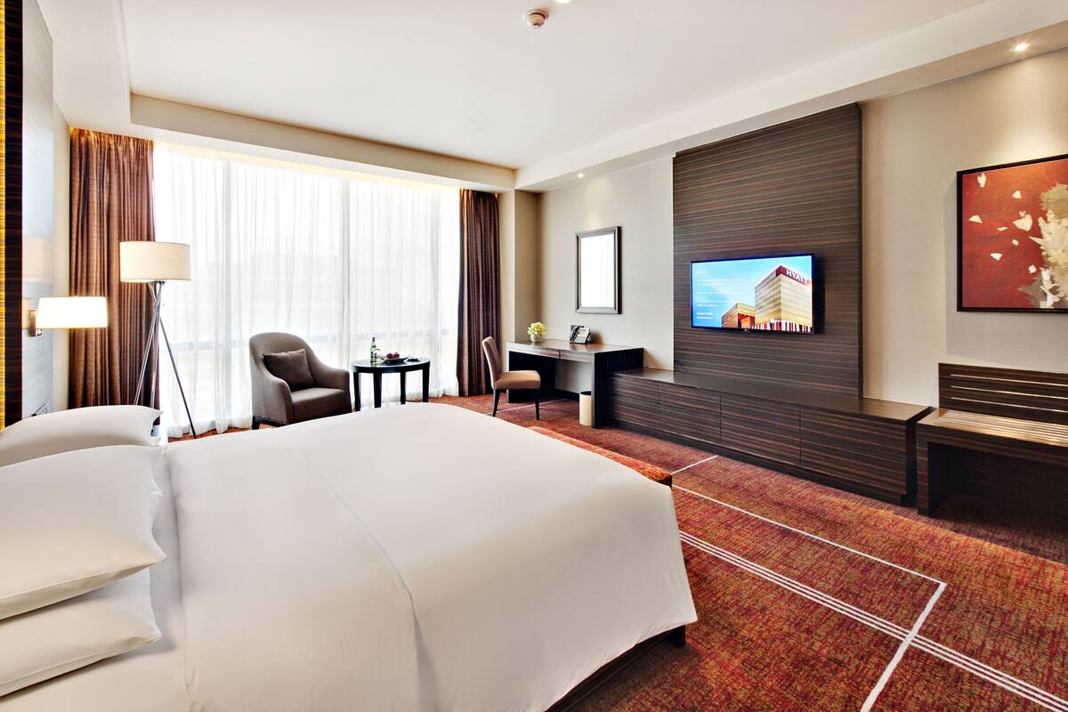 A hotel room with a large bed, a desk, a chair, a TV, and a sofa.