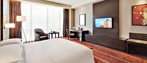 Una habitación de hotel con una cama grande, un escritorio, una silla, un televisor y un sofá.