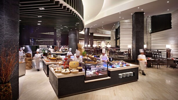 A modern hotel lobby with a central food display, a staircase, and a seating area. - Hyatt Regency Manila, City of Dreams (Parañaque)