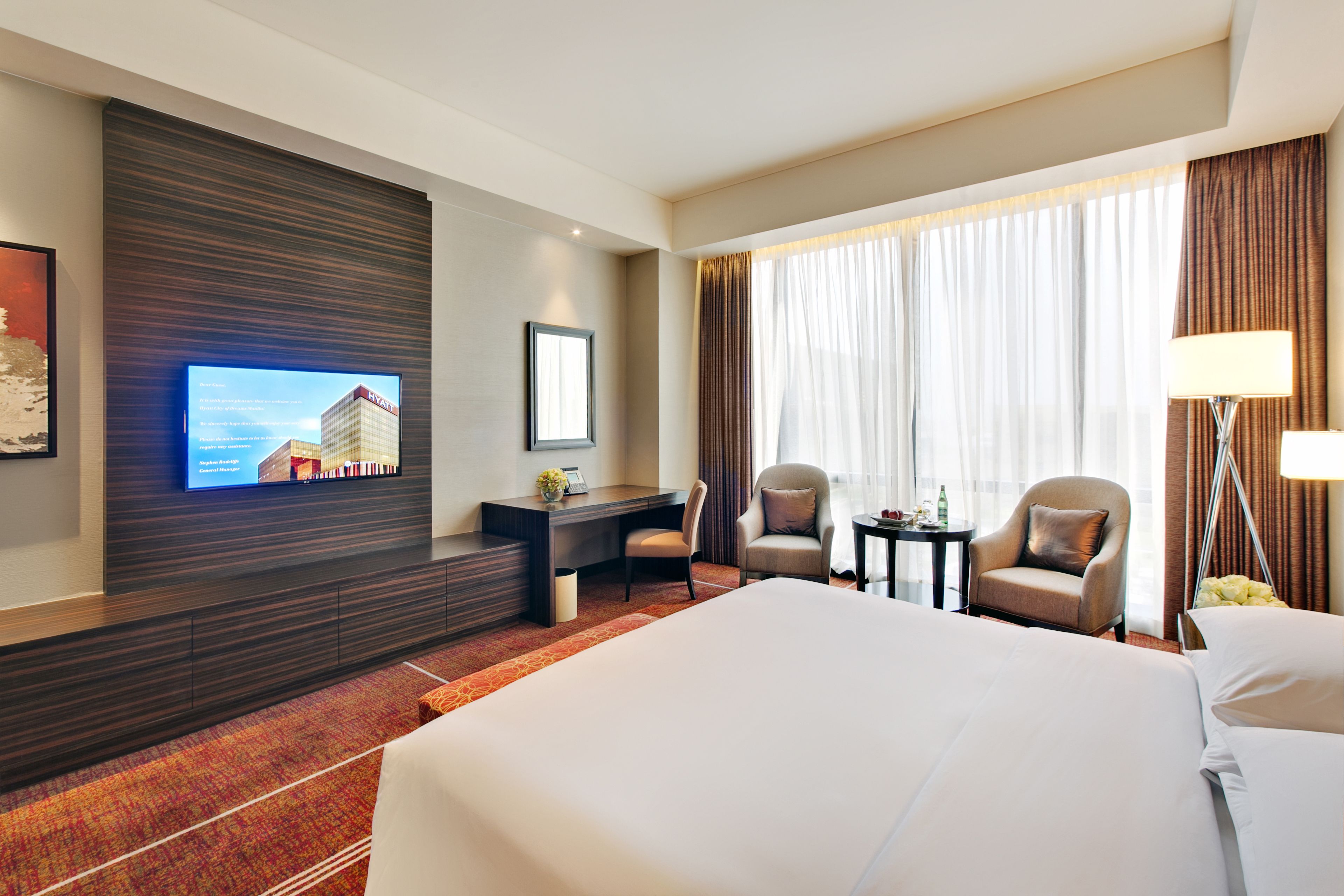 Una habitación de hotel con una cama grande, un escritorio con silla, televisión y ventana con cortinas.