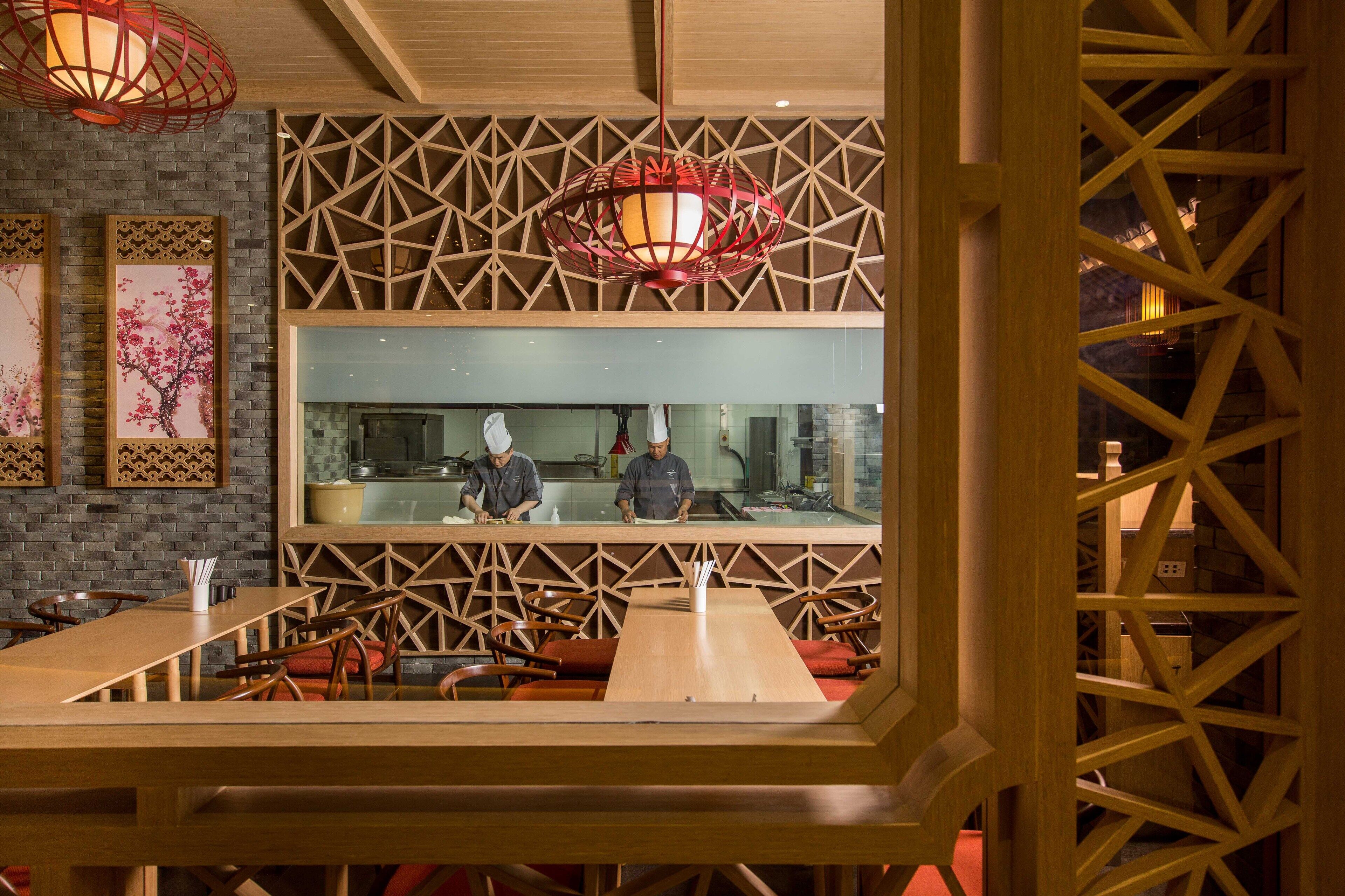 A restaurant interior with a wooden partition, two chefs at the counter, and a red hanging light fixture.