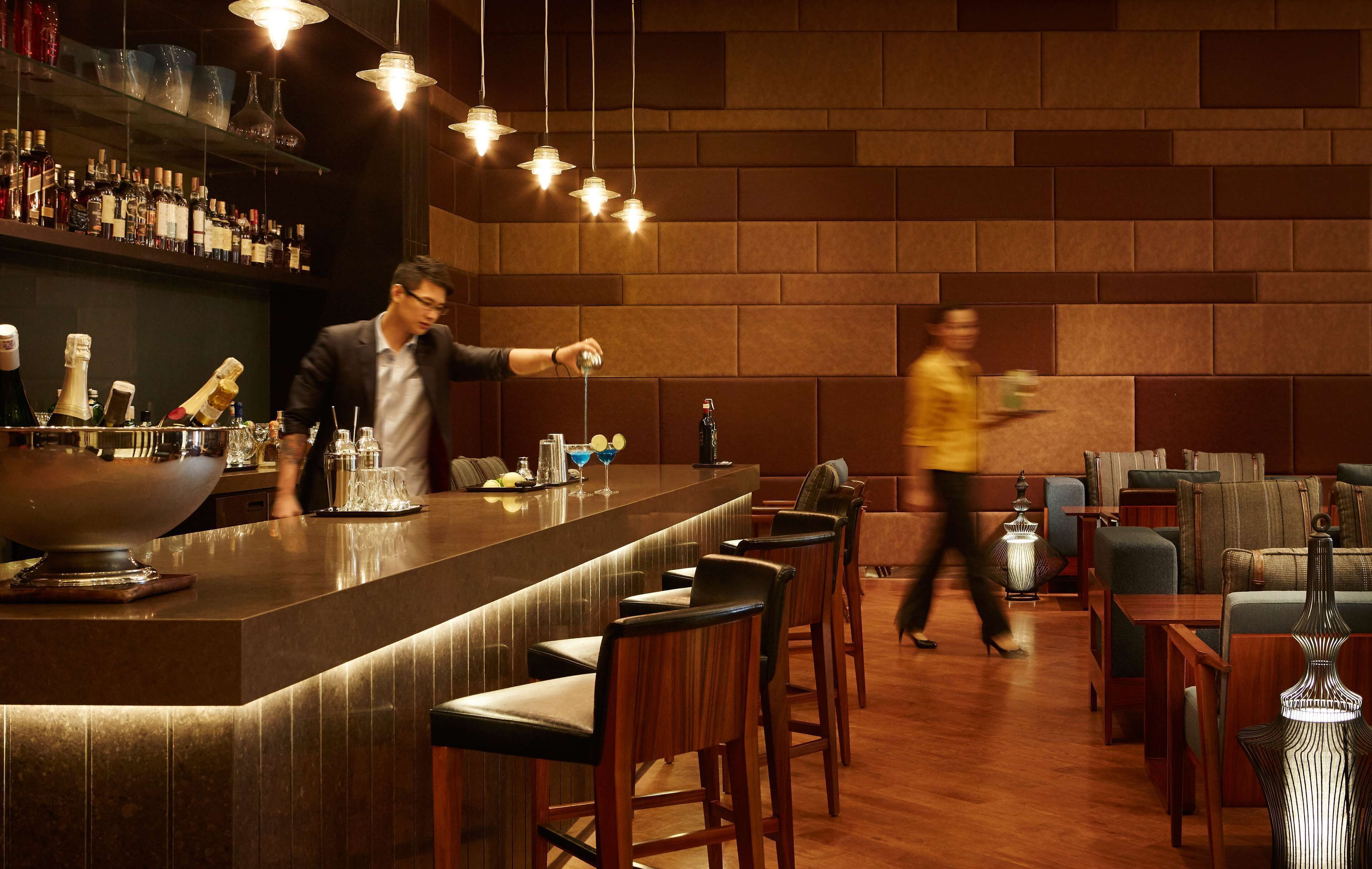 A bar area with a counter, stools, and a bartender. There are tables and chairs in the background.