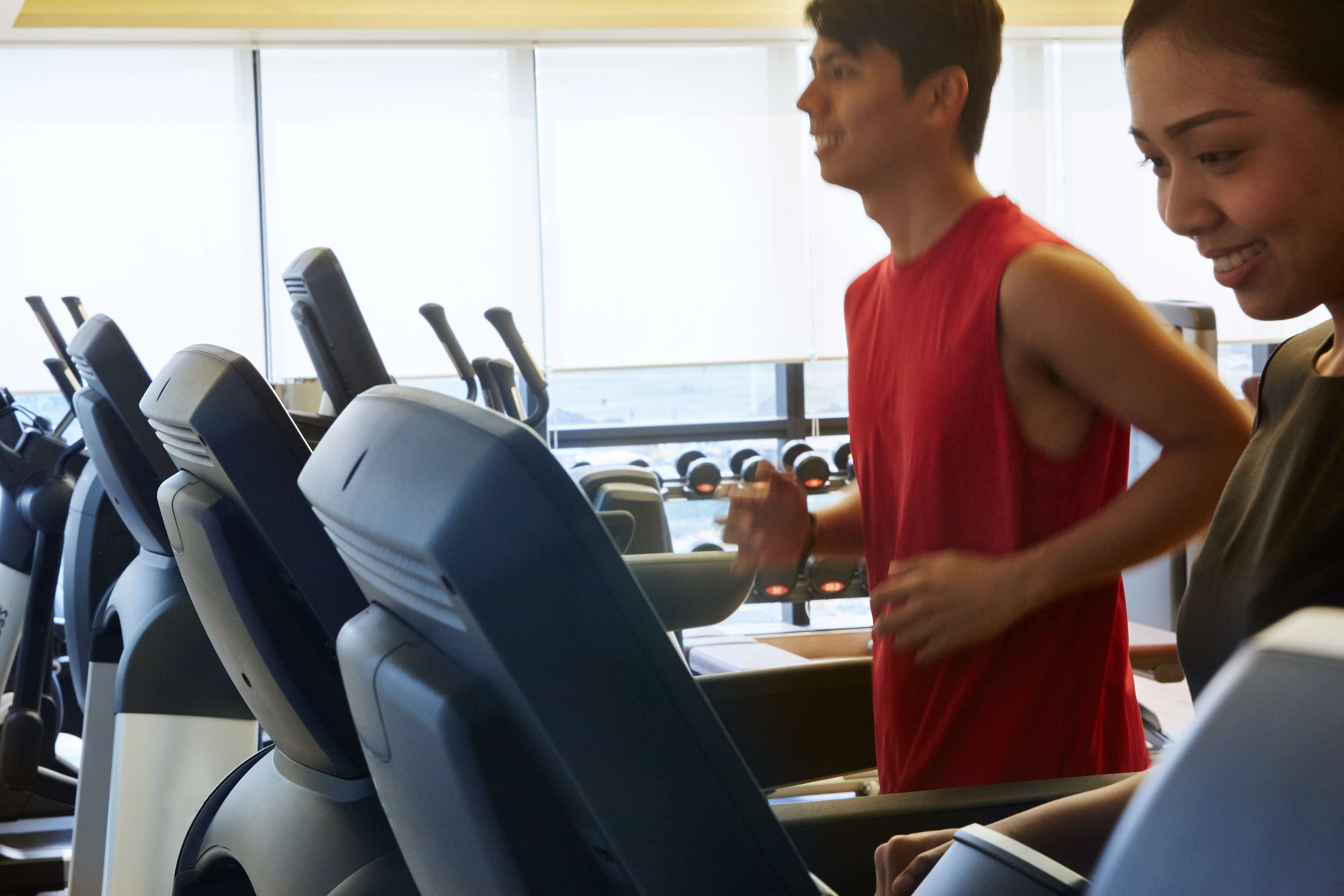 Une salle de sport équipée de matériel d’exercice et une personne courant sur un tapis de course.