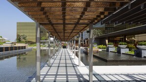 A covered walkway with a reflective floor, leading to a water feature with planters and a modern building in the background. - Hyatt Regency Manila, City of Dreams (Parañaque)