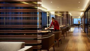 A modern hotel lobby with a long reception desk, comfortable seating, and a view of the city through large windows.