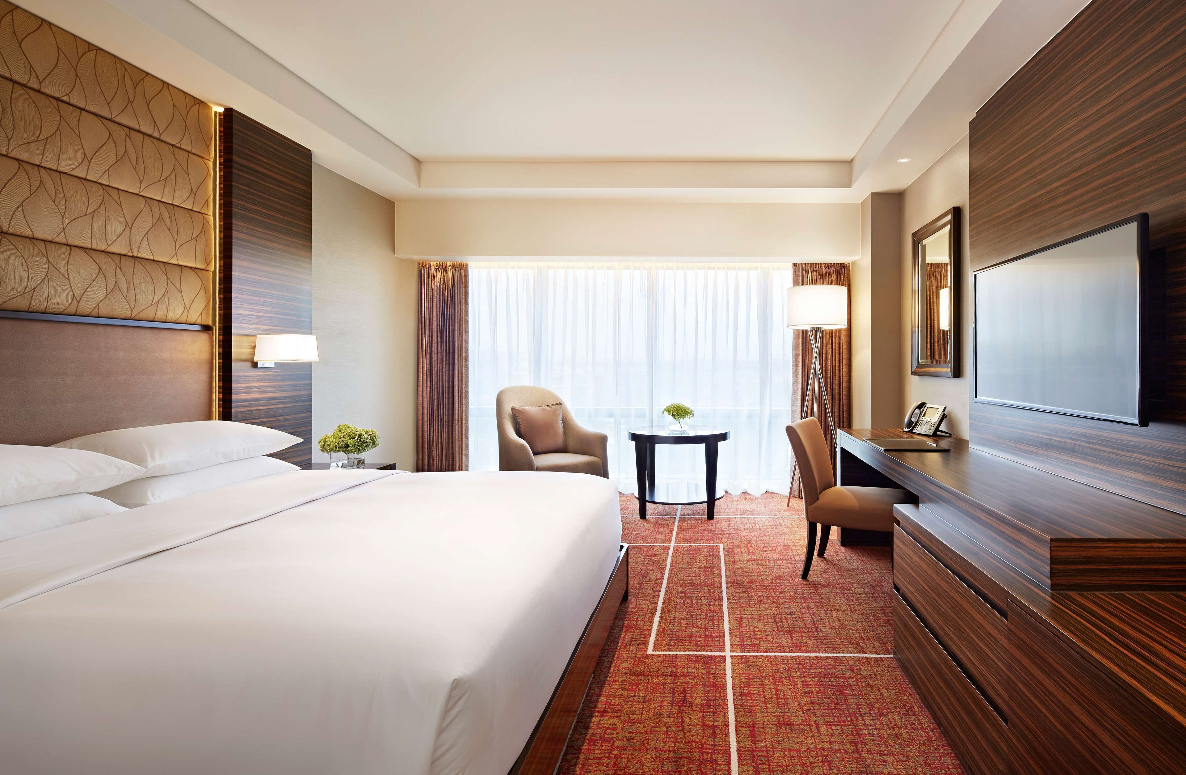 A hotel room with a large bed, a desk with a chair, a TV, and a window with curtains.