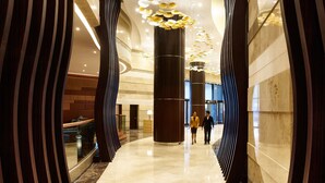 A modern hotel corridor with a reflective marble floor, large wooden columns, and a unique ceiling light fixture. - Hyatt Regency Manila, City of Dreams (Parañaque)