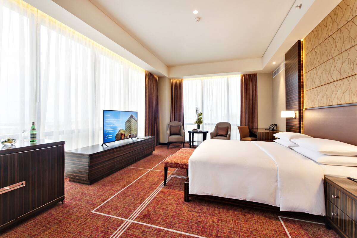 A hotel room with a large bed, a TV, a desk, and a seating area.