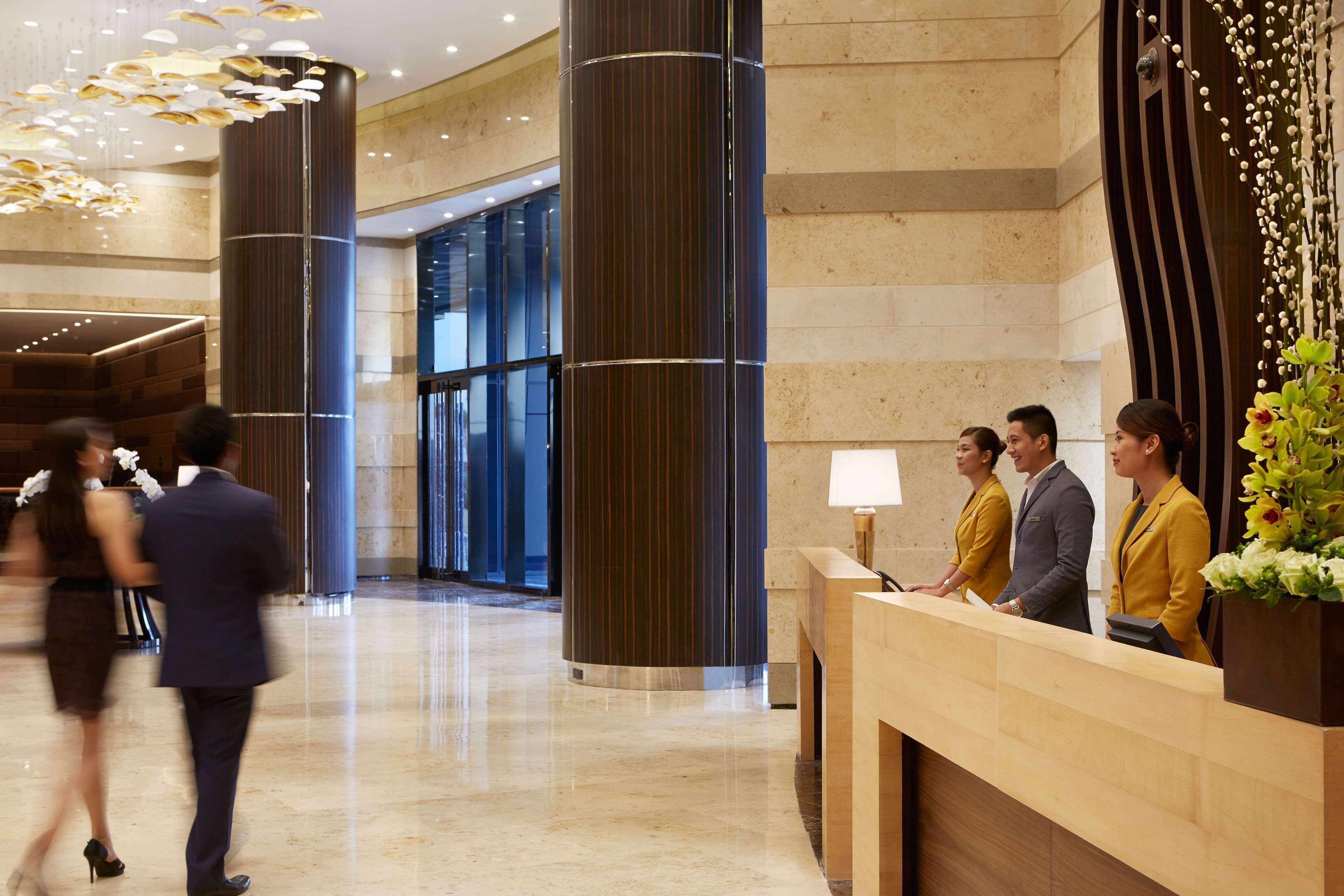 A hotel lobby with a reception desk, large pillars, and a modern chandelier.