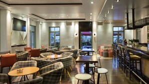 A modern restaurant with a bar area, multiple seating options including bar stools and cushioned chairs, and a large TV mounted on the wall. - Hotel Boschetto (Lefkada)