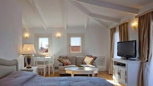 A hotel room with a bed, a sofa, a small dining table, a television, and a window with curtains. - Hotel Boschetto (Lefkada)