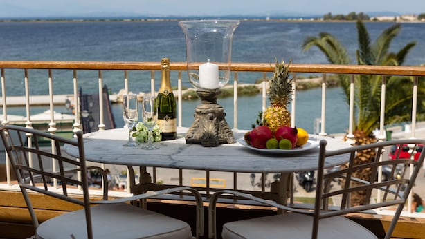 A table with a bottle of champagne, a candle, and a fruit bowl on a balcony overlooking the sea. - Hotel Boschetto (Lefkada)