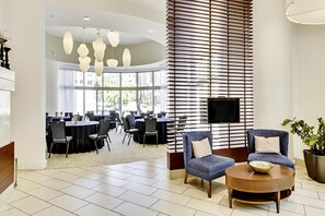 Un hall d’entrée moderne avec un espace salon, un téléviseur fixé sur un mur à lattes et une vue sur la salle à manger grâce à de grandes fenêtres.