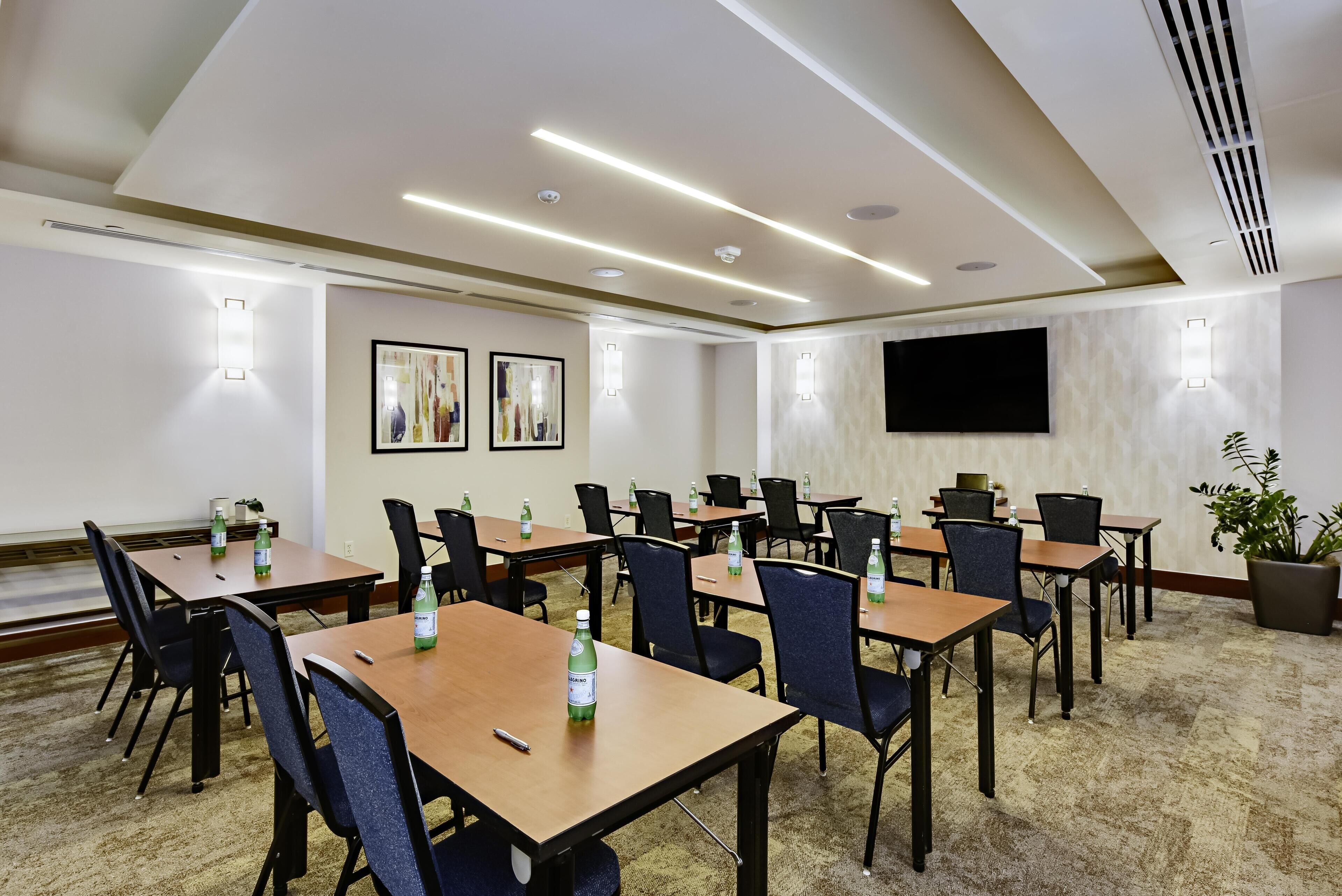 A conference room with tables, chairs, a flat-screen TV, and wall-mounted lights.