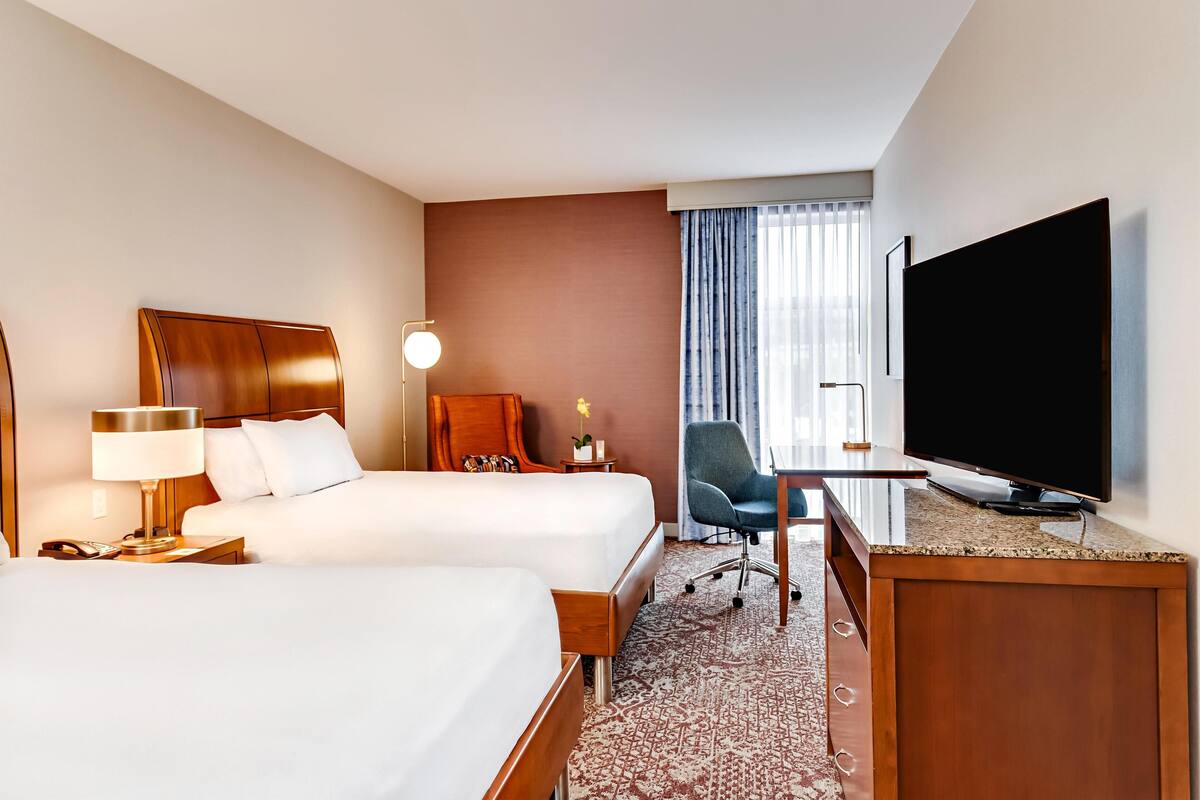 Ett hotellrum med två sängar, ett skrivbord, en tv och en stol.