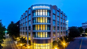 Un hôtel Hilton Garden Inn moderne, doté d’une façade incurvée, de grandes fenêtres et d’une entrée bien éclairée.