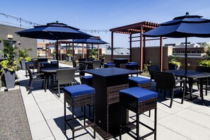 Un espace extérieur aménagé en terrasse, avec plusieurs tables et chaises, protégé par des parasols et entouré de plantes en pot.