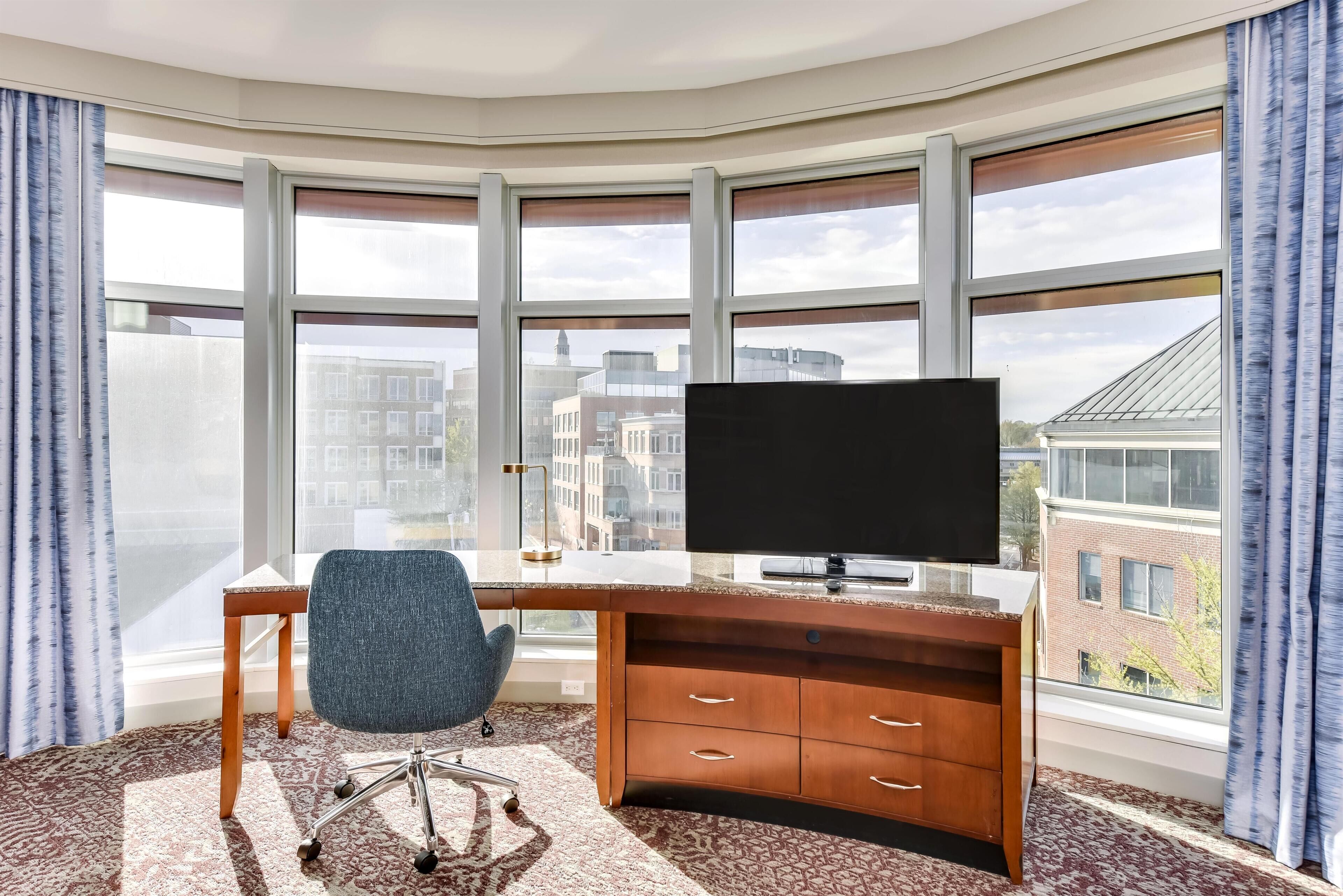 A modern office space with a large desk, chair, and a flat-screen TV.