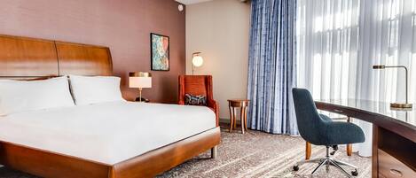 Habitación de hotel con una cama grande, un escritorio, una silla, una mesita y una ventana con cortinas.