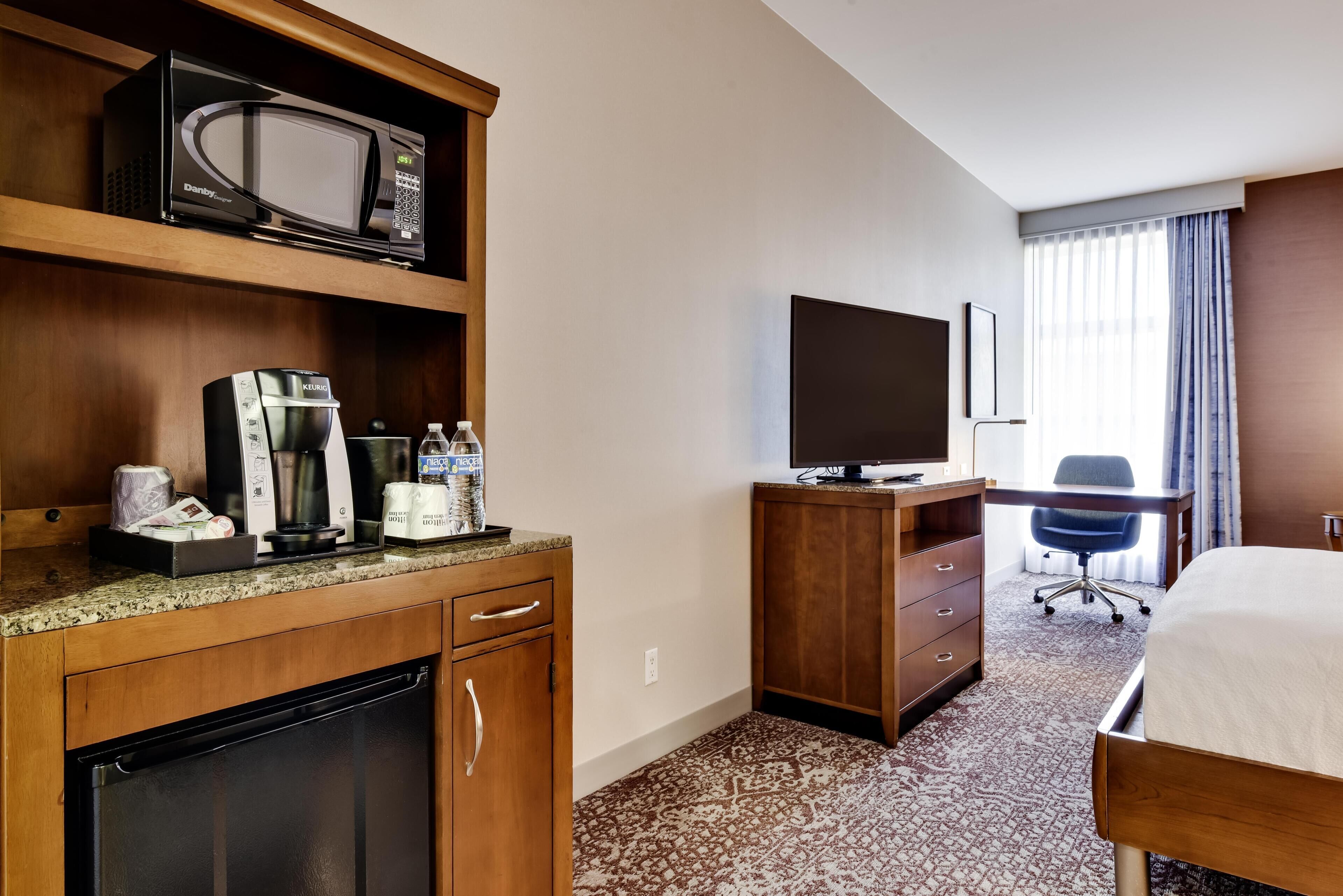 Una habitación de hotel con kitchenette, televisión, cama y escritorio.