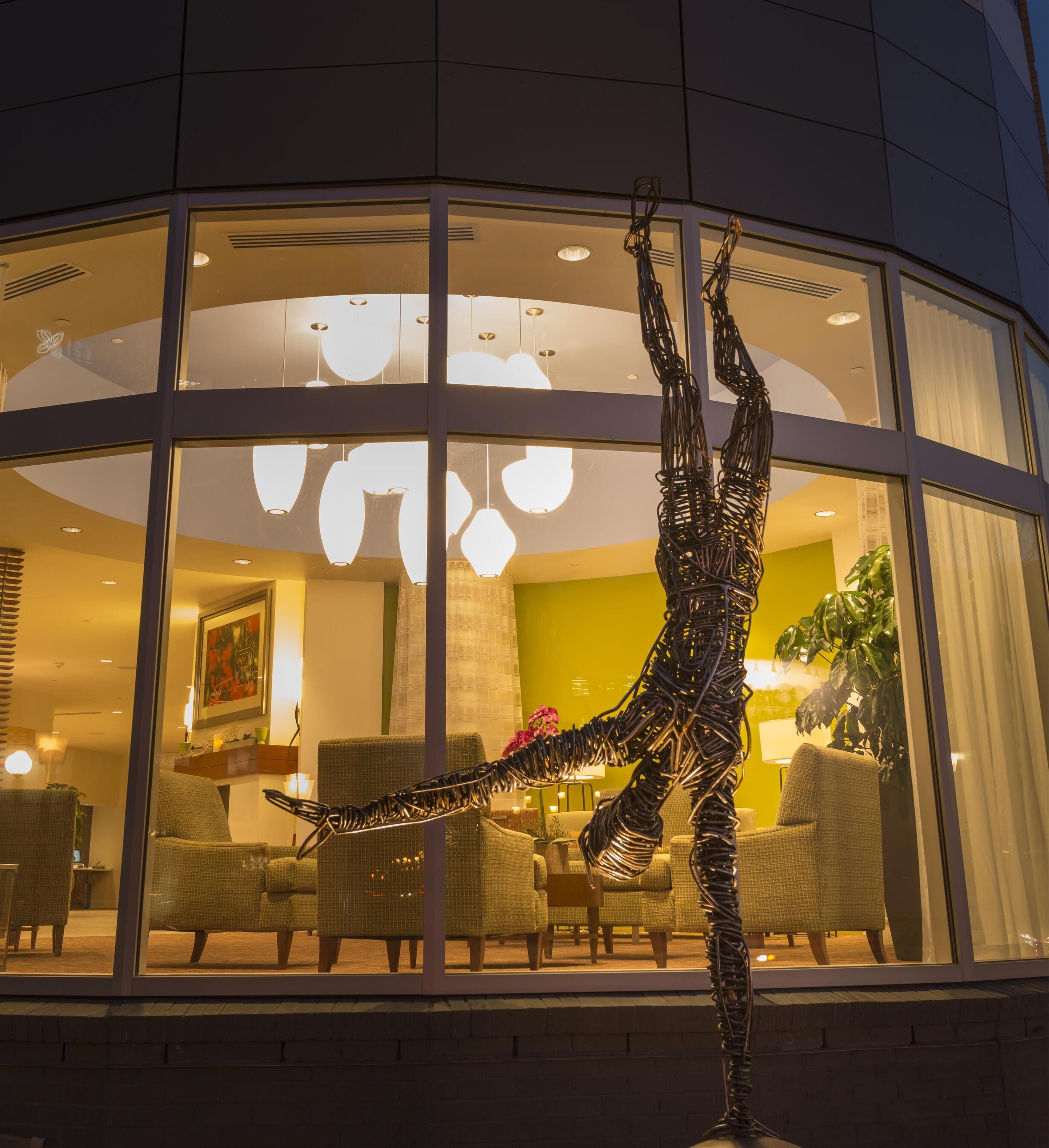 Een modern hotelinterieur met een groot raam, rieten meubels en een uniek metalen sculptuur.