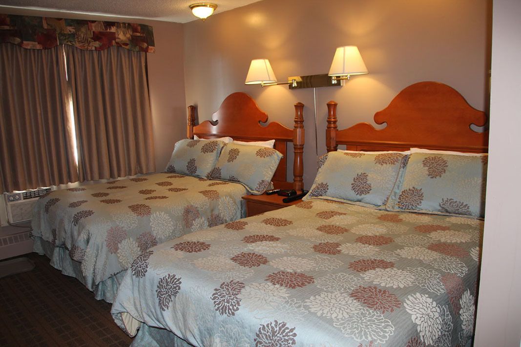 Une chambre d’hôtel avec deux lits, chacun agrémenté de draps à motifs floraux, d’une tête de lit en bois et de deux lampes fixées au mur.