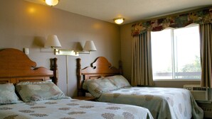Habitación de hotel con dos camas, cada una con ropa de cama estampada con motivos florales, cabeceros de madera, mesitas de noche, lámparas y una ventana con cortinas.