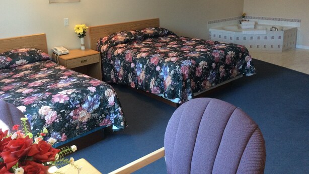 A hotel room with two beds, a sofa, a bedside table, a phone, and a vase with flowers. - Rainbow Motel (Swift Current)
