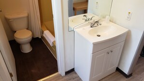 A bathroom with a toilet, sink, mirror, and wooden floor. - Rainbow Motel (Swift Current)