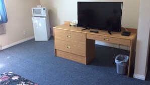 A room with a wooden desk, a television, a microwave, and a trash can. - Rainbow Motel (Swift Current)